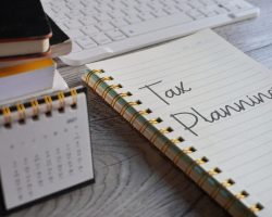 Closeup image of notebook with text TAX PLANNING and calendar on office desk. Business and financial concept